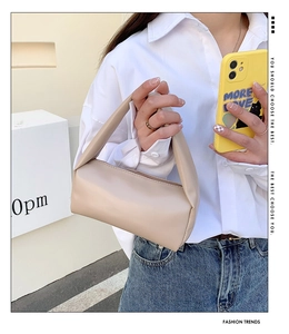 Detail view of a beige cylindrical handbag held by a model in casual white shirt and jeans