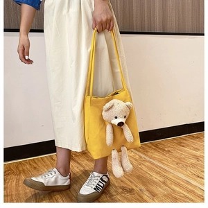 Detail of yellow canvas tote bag featuring a 3D plush teddy bear and dual shoulder straps