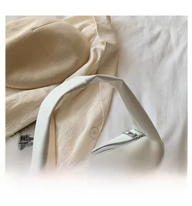 Detail of minimalist white leather handbag with ruched strap and silver zipper closure