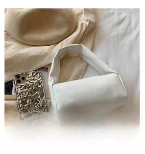 Detail of soft white puffed handbag and silver metallic phone case on a hat