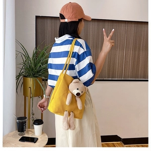 Close-up of bright yellow canvas tote with 3D plush bear detail worn by a model