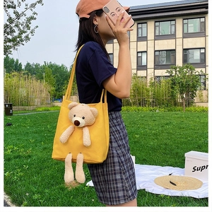 Detail view of bright yellow canvas shoulder bag with 3D teddy bear plush accessory