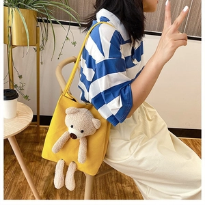 Detail of yellow canvas bag featuring a 3D plush bear on the front with shoulder strap