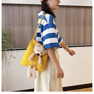 Side view of a yellow canvas shoulder bag featuring a 3D plush bear on a model