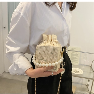 Detail of woven straw bucket bag with floral embroidery and pearl carry handle