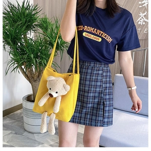 Detail of yellow canvas tote bag with 3D plush bear being worn by a model in lifestyle setting