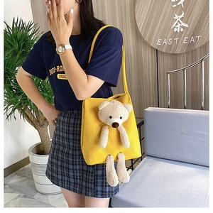 Detail showing the 3D plush bear on a yellow canvas tote bag worn by a model