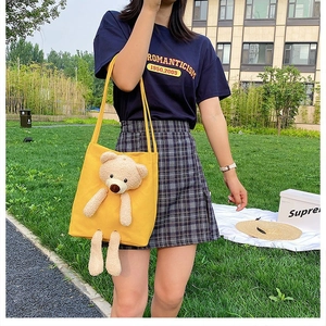 Detail of a bright yellow canvas tote bag featuring a 3D plush bear on a grass background