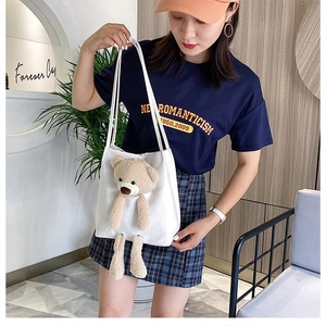Detail of white canvas tote bag featuring a 3D plush bear doll and long shoulder straps