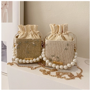 Detail view of woven bucket bag featuring pearl handle, floral embroidery and gold chain