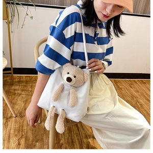 Detail of white canvas shoulder bag with a 3D plush bear on a striped model outfit