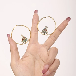 Detail of gold hoop earrings with sparkling zircon Christmas tree charms held by hand