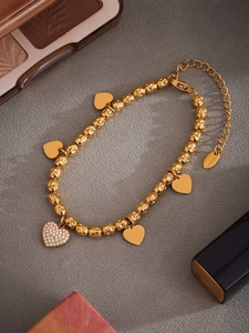 Macro shot of gold stainless steel beaded bracelet with five heart charms and pavé zircon