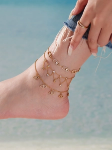 Gros plan de bracelets de cheville dorés avec charms oeil et pompons au bord de la mer