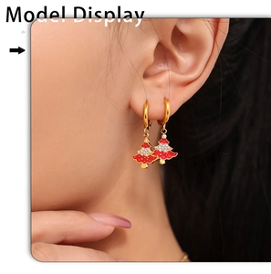 Detailed view of red enamel Christmas tree drop earrings with gold hoops on a model