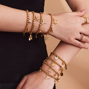 Gold stainless steel beaded bracelet with starfish and heart charms on a female wrist