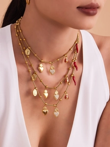 Détail d'un collier doré multicouche avec breloques cœur, pièce et piment rouge