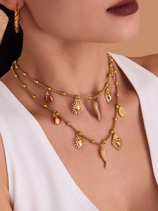 Model wearing a layered gold charm necklace with ladybug and red pepper pendants