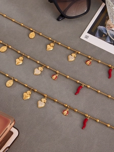 Détail de colliers en perles dorées avec pendentifs cœur et coccinelles rouges