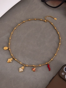 Détail du collier en acier doré avec pendentifs cœur, coccinelle et piment
