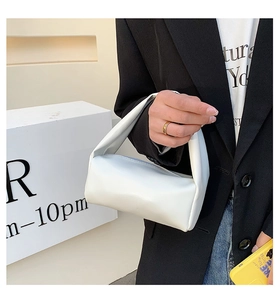 Detailed view of a white minimalist cylindrical handbag made of soft leather held by a model