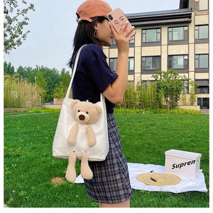 Detail view of white canvas tote bag featuring a 3D plush teddy bear and shoulder strap