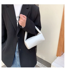 Minimalist white cylindrical bag shown in a lifestyle scene against a black blazer