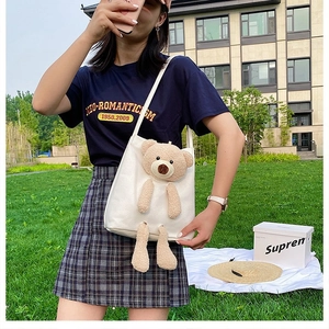Detail of white canvas tote featuring a 3D plush bear mascot on bright outdoor grass