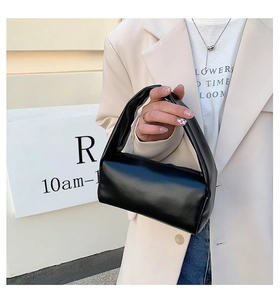 Detail of a black leather cylinder bag with wide handle shown in a lifestyle street setting