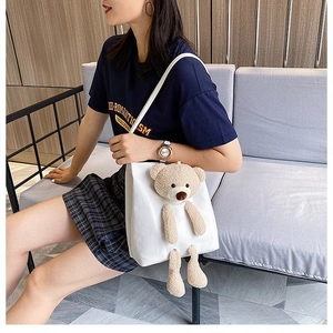 Detail shot of white canvas shoulder bag featuring a 3D plush teddy bear decoration