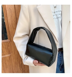 Close-up of minimalist black leather cylinder handbag with soft texture and wide strap