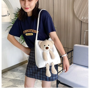Detail of white canvas tote bag featuring a 3D plush bear and adjustable shoulder strap