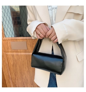 Minimalist black cylinder handbag with smooth leather texture held by a model in a beige suit