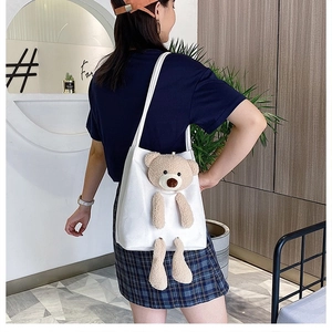Close-up of white canvas tote featuring a 3D plush bear ornament on a shoulder bag strap