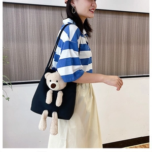 Detail of black canvas tote bag with a 3D plush teddy bear and slim shoulder strap