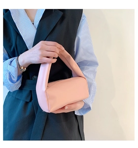 Detailed close-up of a soft pink minimalist cylinder handbag held by a model