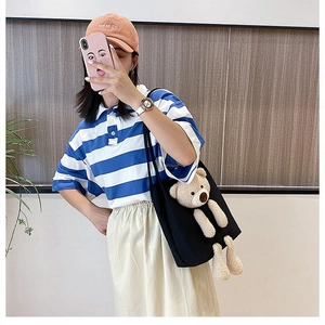 Lifestyle view of a black canvas tote bag featuring a 3D plush bear with casual outfit