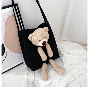Detail of black canvas tote bag featuring a cute 3D plush bear doll and shoulder strap