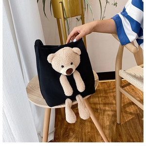 Detail of a black canvas tote bag featuring a cute 3D plush bear on a wooden chair