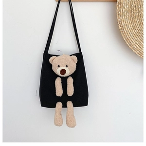 Detailed view of a black canvas tote bag featuring a 3D plush bear doll on a clean wall