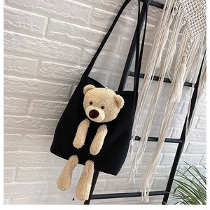 Detail of black canvas tote featuring a 3D plush teddy bear mascot with a shoulder strap