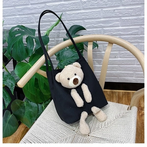 Detail of 3D plush bear on black canvas tote bag hanging on a wooden chair