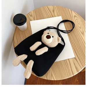 Detailed view of black canvas crossbody bag with 3D plush bear on a wooden surface