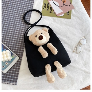Detail of a black canvas bag with a cute plush brown bear and round rope strap on white fabric