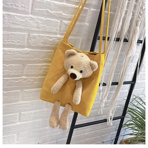 Detail of yellow canvas tote bag featuring a 3D plush bear on white brick wall