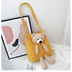Close-up of yellow canvas shoulder bag featuring a 3D plush teddy bear and double straps