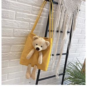Detail of yellow canvas tote bag featuring a 3D plush teddy bear and shoulder straps