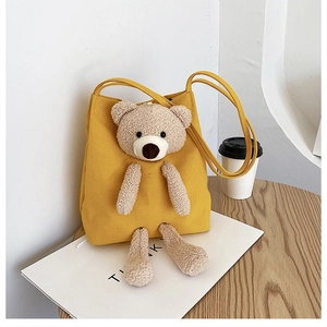 Detail of yellow canvas tote bag featuring a 3D plush bear on a wooden cafe table