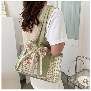 Dettaglio della borsa in paglia intrecciata con ricami floreali rosa e fiocco in pizzo