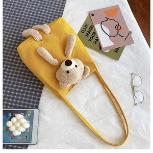 Detail of yellow canvas tote bag featuring a 3D plush teddy bear and soft fleece texture